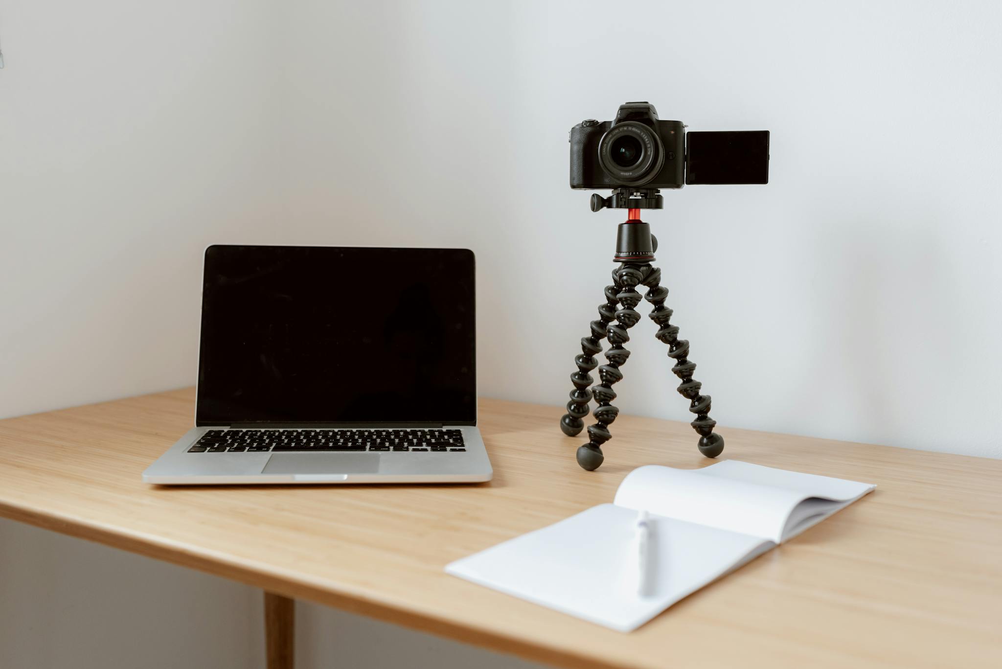 Modern workplace consisting of netbook camera on tripod near opened planner with pen on wooden table